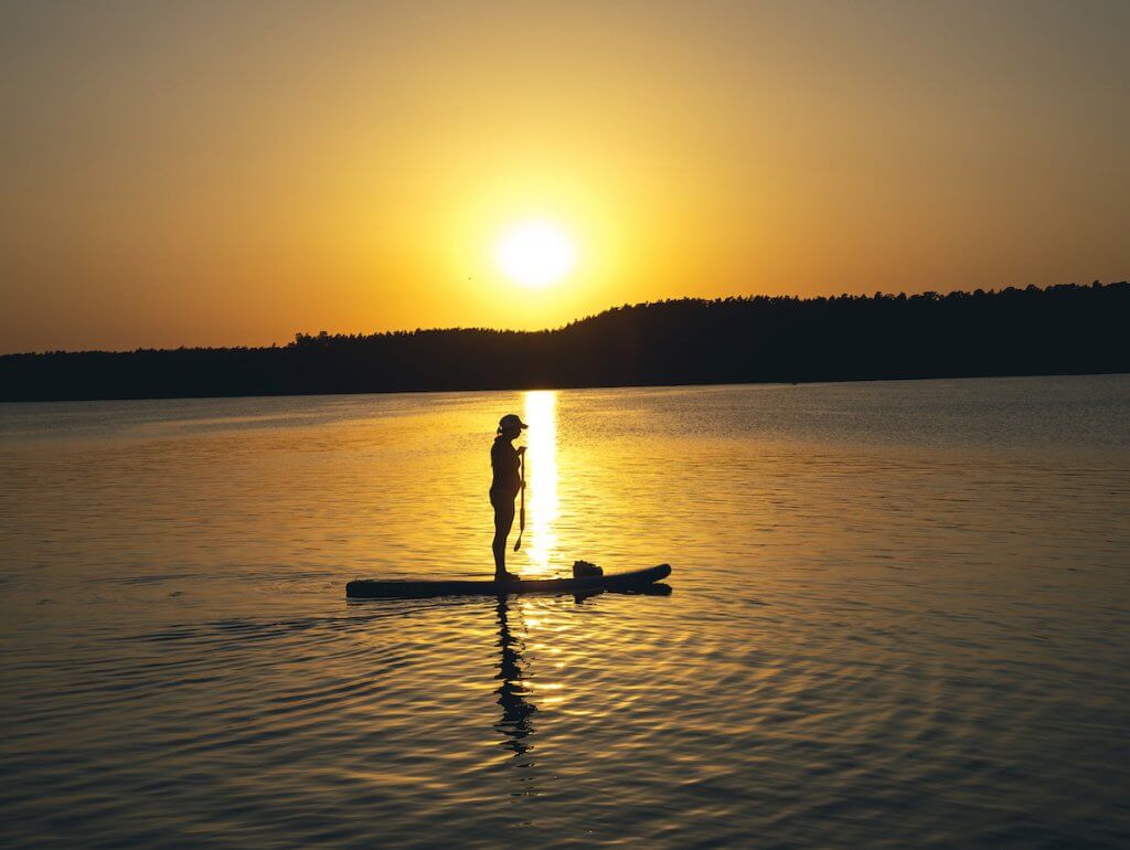 dziewczyna pływa na desce SUP po jeziorze o zachodzie słońca